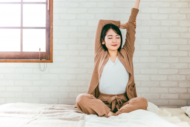 ベッドの上で座ってストレッチをする女性