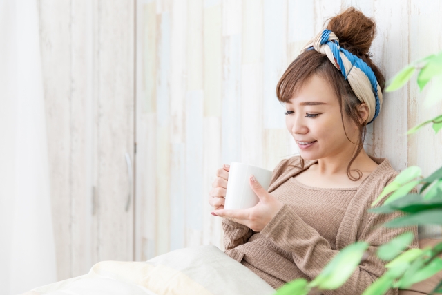 ベッドで温かい飲み物を飲む女性