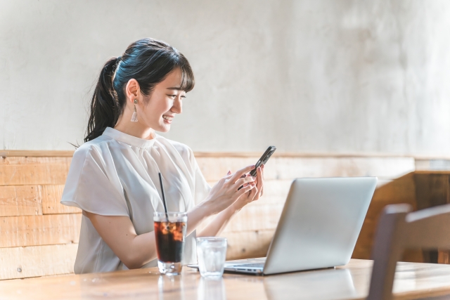 冷たい飲み物をPCのそばに置きデスクワーク中の女性